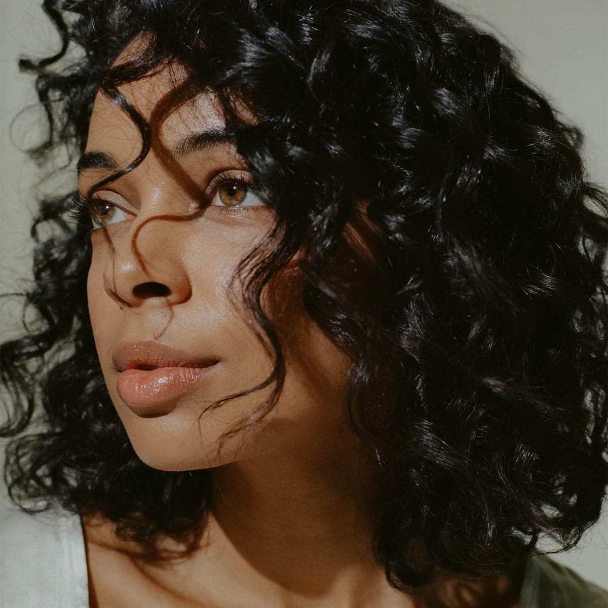A close-up of a woman with voluminous, dark, curly hair using 14th Night Natural Surf Spray