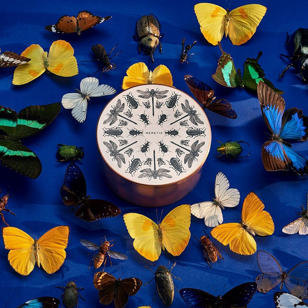 Heretic Parfum The Entomologist Candle (15 oz) - product shown on blue background with butterflies surrounding it.