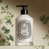 Diptyque Comforting Moisturizing Lotion (350 ml) - product shown on counter with leafy background.