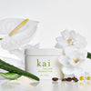 Kai Fragrance Body Polish (8 oz) - product shown with flowers around it.