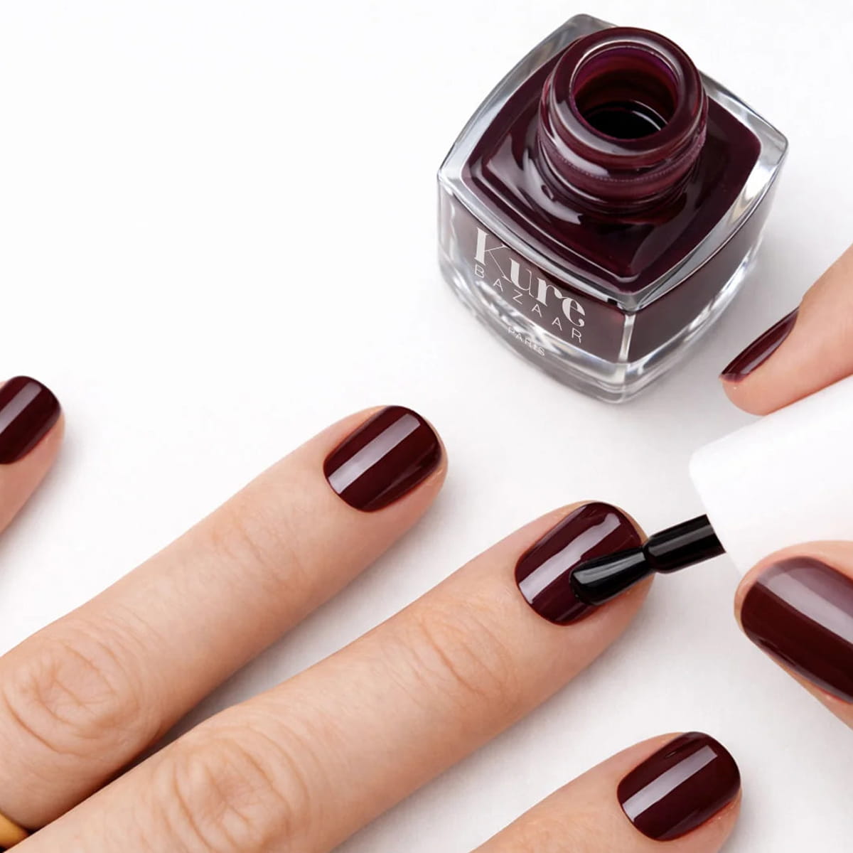 Kure Bazaar Nail Lacquer - Burgundy (10 ml) - product shown being applied to nails.