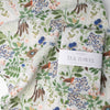 A folded Botanica Paper Co. Flowering Trees Tea Towel (1 pc) sitting on top of Botanica Paper Co. Flowering Trees Tea Towel shown flat