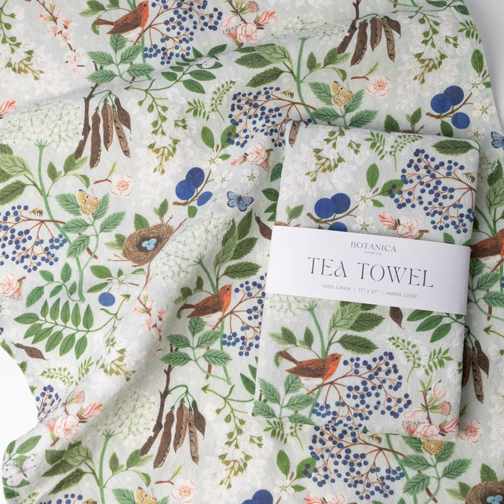 A folded Botanica Paper Co. Flowering Trees Tea Towel (1 pc) sitting on top of Botanica Paper Co. Flowering Trees Tea Towel shown flat