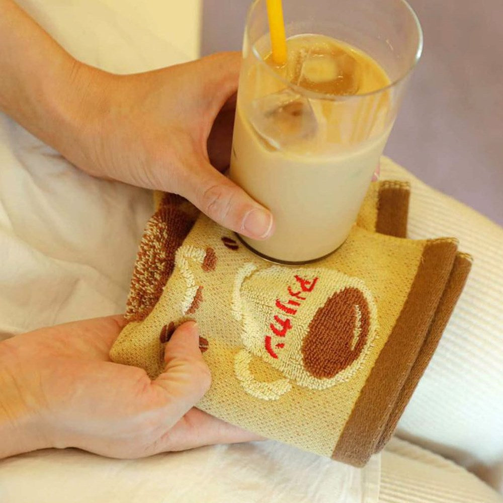 A close-up of hands holding a clear glass of iced coffee over a Hightide Hand Towel - Coffee (1 pc)