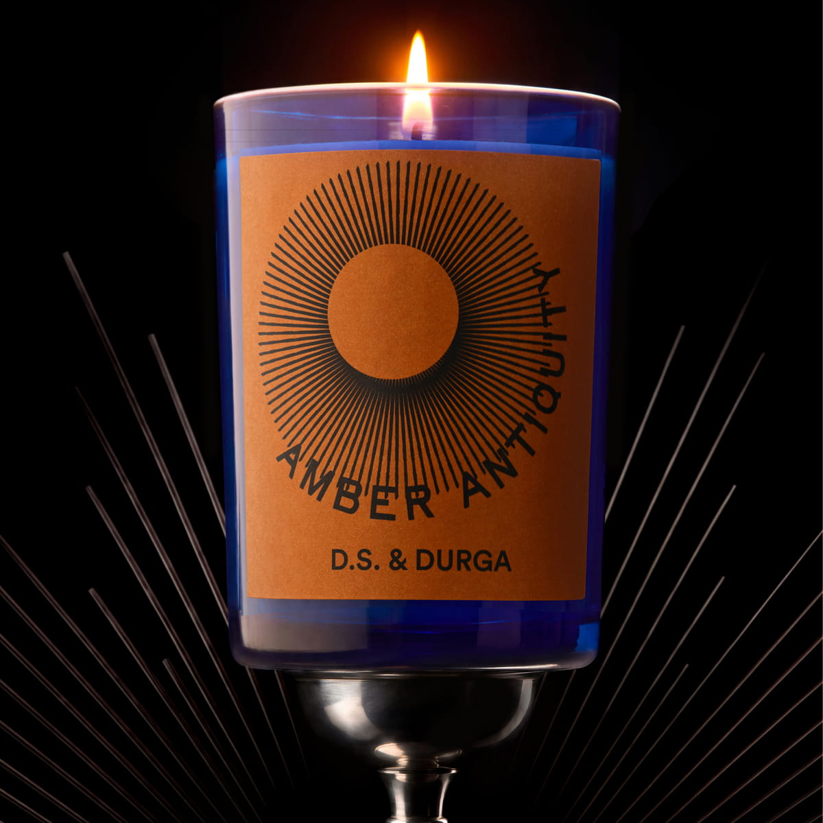 Lifestyle shot of D.S. & Durga Amber Antiquity Candle (7 oz) shown with flame and starburst rays in the background