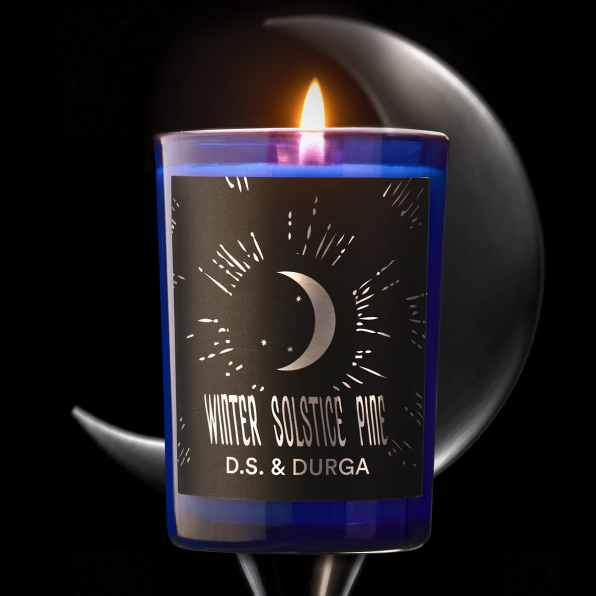 Lifestyle shot of D.S. & Durga Winter Solstice Pine Candle (7 oz) shown with flame on a pedestal with a crescent moon in the backround