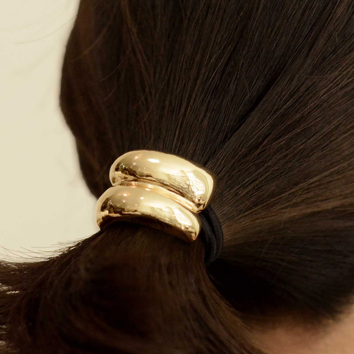 A close-up of a person's dark brown hair tied back with nar’sha Mini Double Arch Metal Ponytail Hair Tie - Gold