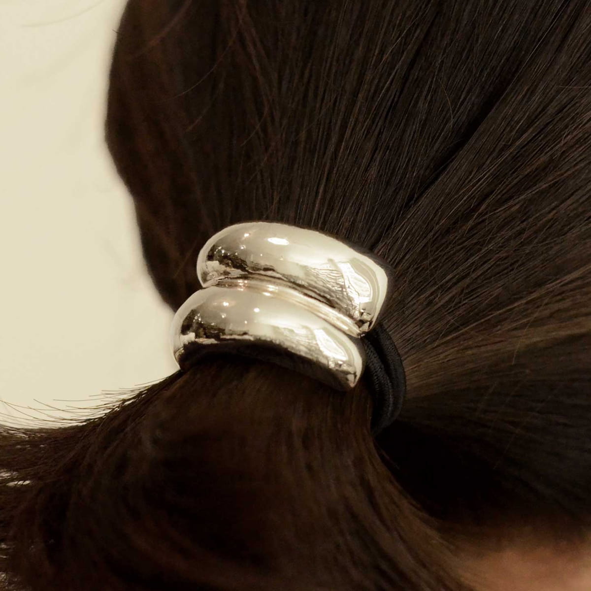 A close-up of a person's dark brown hair tied back withnar’sha Mini Double Arch Metal Ponytail Hair Tie - Silver