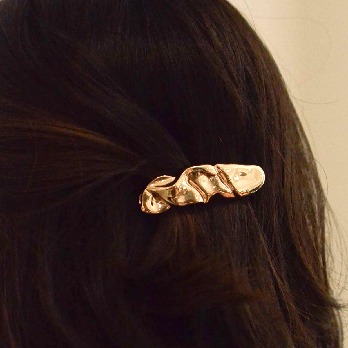 A close-up of a person's dark brown hair secured with a nar’sha Textured Metal Barrette Hair Clip - Gold