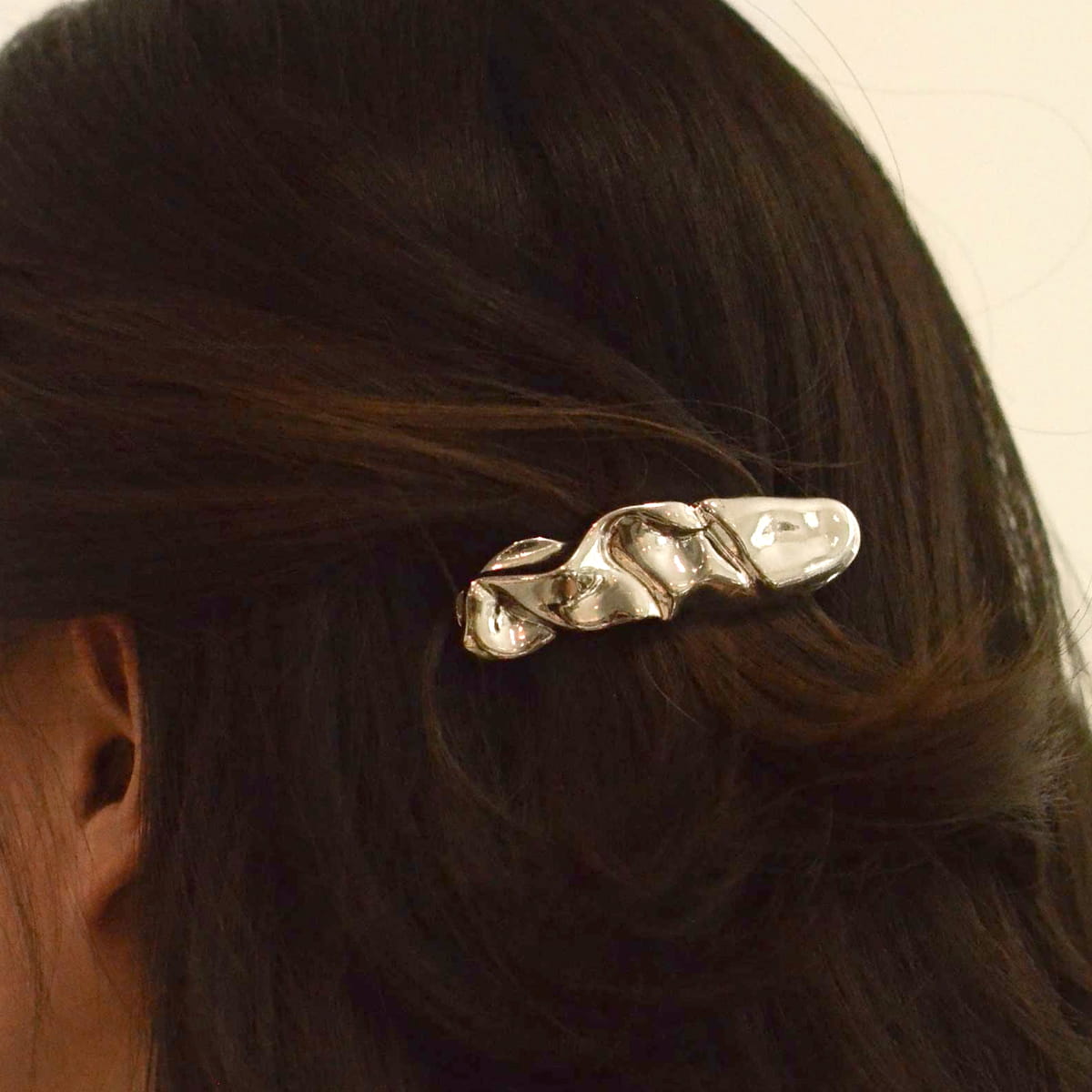 A close-up of a person's dark brown hair secured with a nar’sha Textured Metal Barrette Hair Clip - Silver