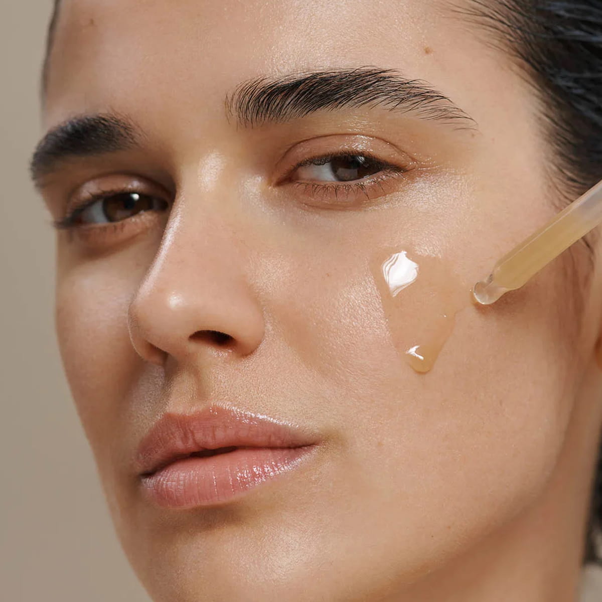 Close-up of a woman's face with a clear dropper applying Dr. Hauschka Hydrating Serum Plus