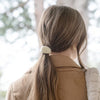 A woman viewed from behind wearing an L. Erickson Buena Vista Pony Cuff - Cream in her brown ponytail, with a blurred outdoor background