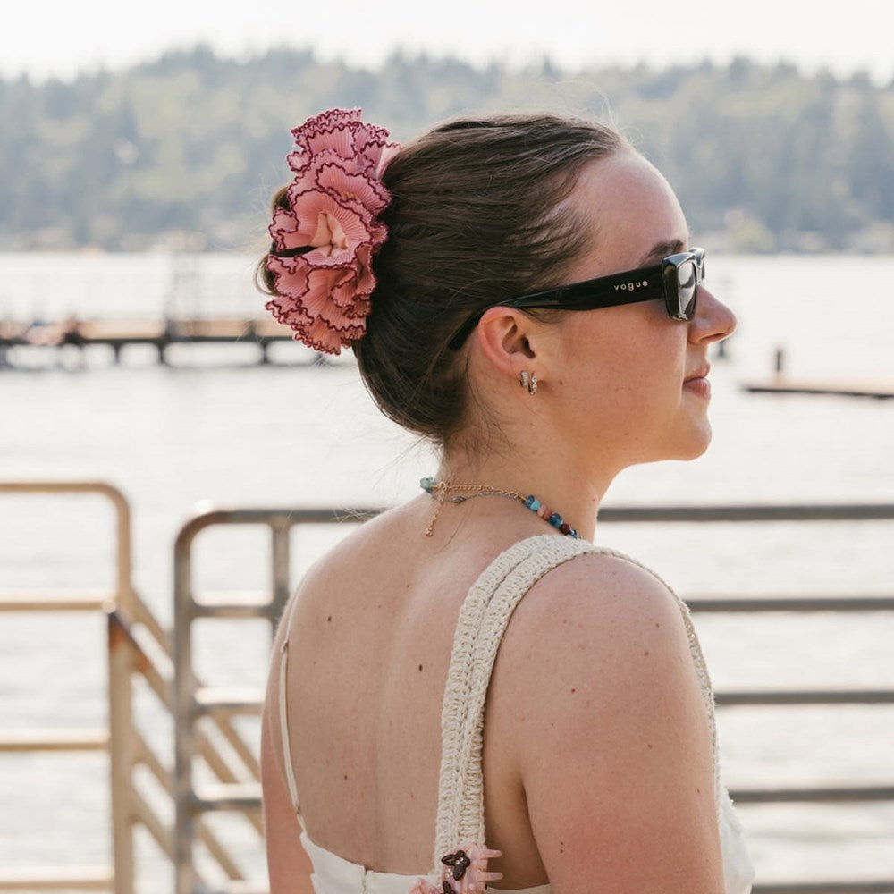 A woman in profile wearing L. Erickson Lilo Scrunchie in her hair, standing outdoors near a waterfront with a railing and trees in the background