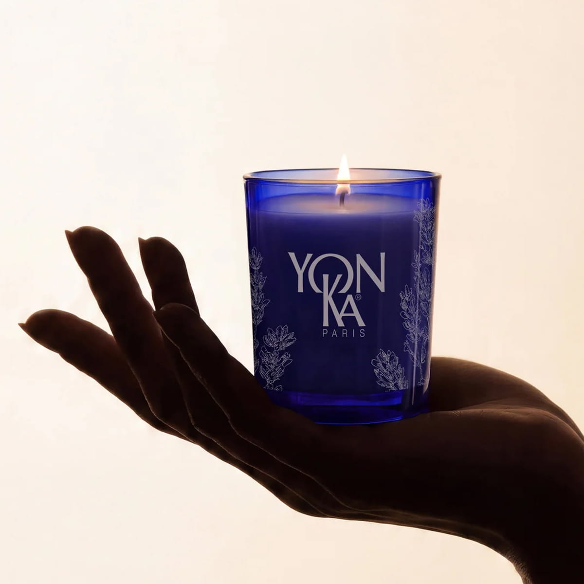 Yon-Ka Lavender Scented Candle held in the palm of a person's hand against a warm off-white background.
