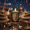 Diptyque Limited Edition Sapin (Pine Tree) Classic Candle (190 g) with a lit flame sits in a whimsical, toy-like scene featuring wooden animals, star-shaped ornaments, and a dark blue background.
