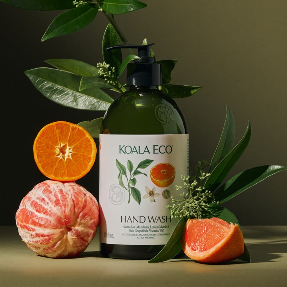 Koala Eco Hand Wash - Mandarin, Lemon Myrtle and Pink Grapefruit (Glass Bottle) (16.9 oz), styled with mandarin fruit halves and green leaves on a dark olive background.