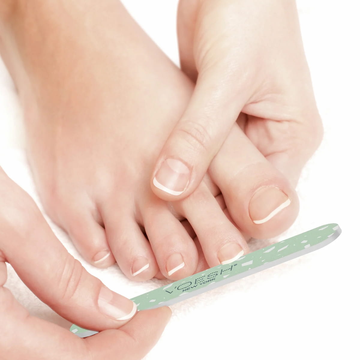 A close-up of a person's feet and hands using a mint green VOESH nail file on their toenails against a white background.