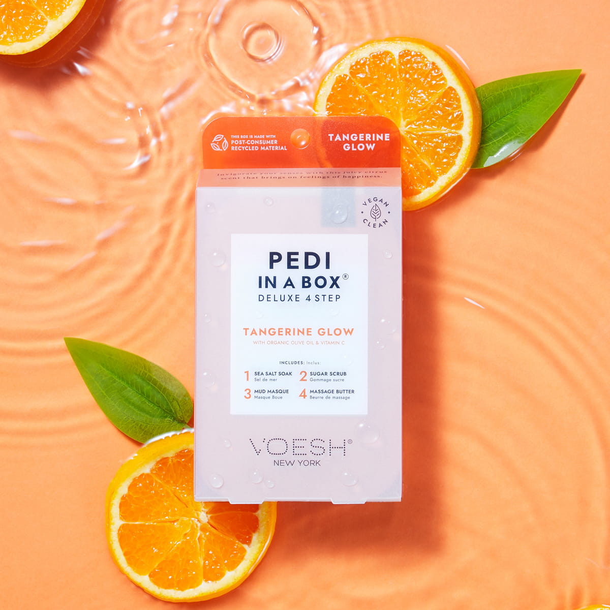 VOESH New York Pedi In A Box - Tangerine Glow box styled on a peach background with water ripples, orange slices, and green leaves.