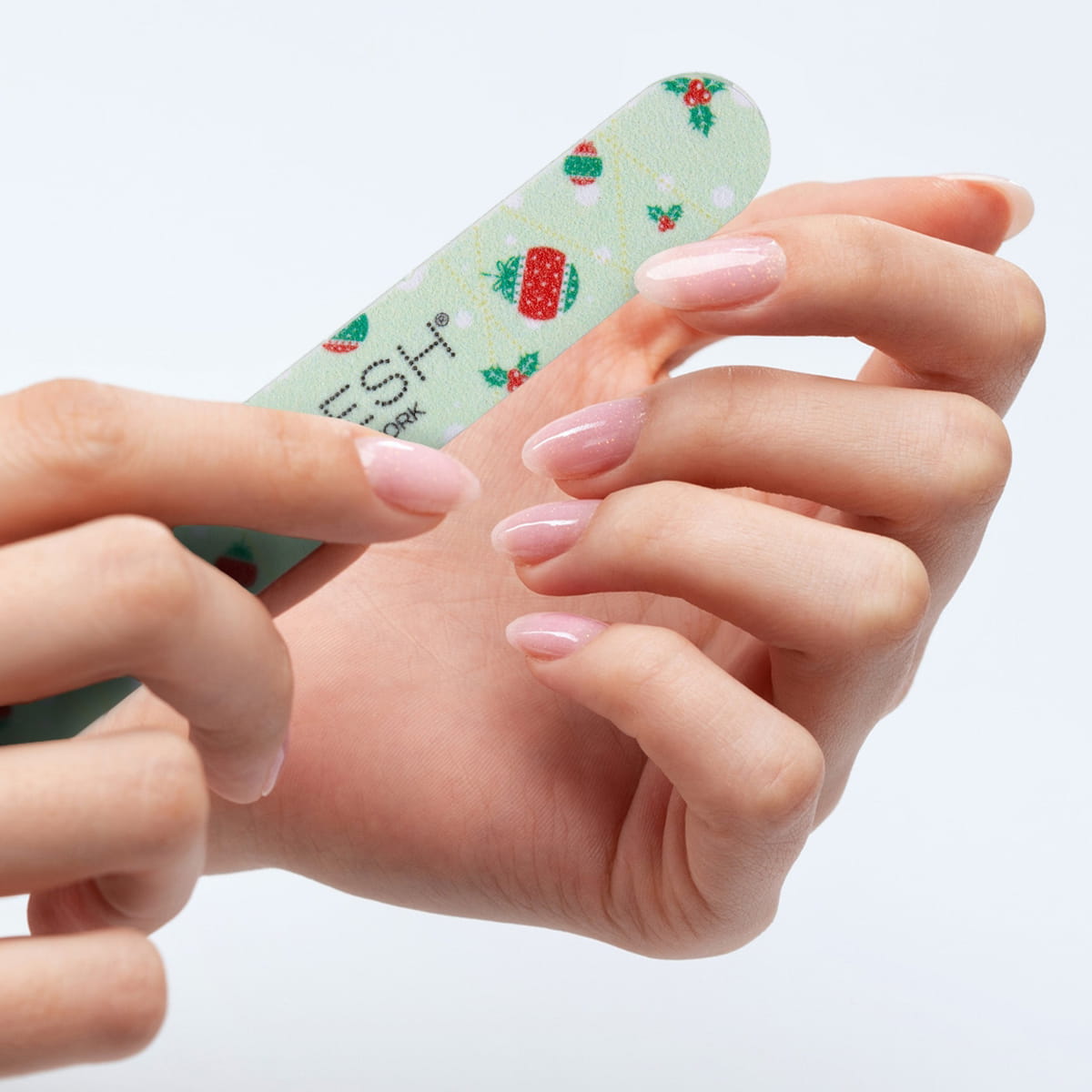 A close-up of hands with manicured pink nails using the holiday theme nail file from the VOESH New York Mini Mani Set