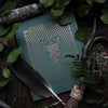 Lifestyle shot of Open Sea Agnes’ Grimoire Notebook (1 pc) showing cover with feather and leaves in the background