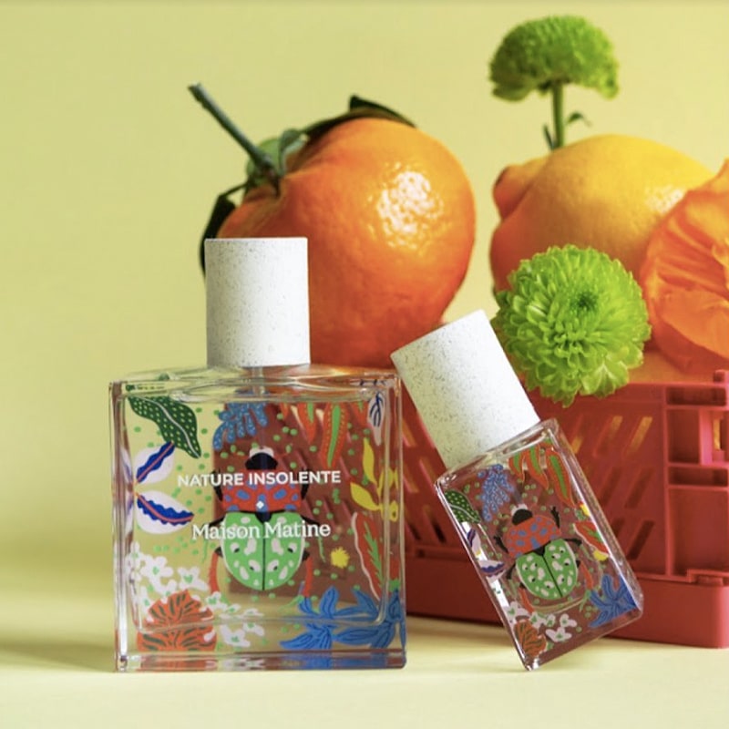Lifestyle shot of Maison Matine fragrance in two sizes with orange, lemon and green flowers in the background