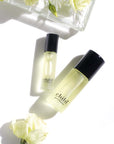 Beauty shot of Child Perfume Roll On with both size bottles with white flowers and white roses in the background