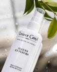 Lifestyle shot of Leonor Greyl Algues et Fleurs Conditioner Curl Enhancer Styling Spray (150 ml) with leaves in the background