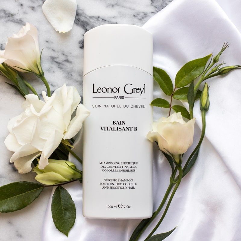Lifestyle shot top view of Leonor Greyl Bain Vitalisant B Shampoo (200 ml) with white roses in the background