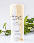 Lifestyle shot of Leonor Greyl Banane Shampoo Bain Restructurant a la Banane (200 ml) with shampoo pouring over bottle and leaves in the background