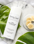 Lifestyle shot top view of Leonor Greyl Banane Shampoo Bain Restructurant a la Banane (200 ml) with banana slices and leaves in the background
