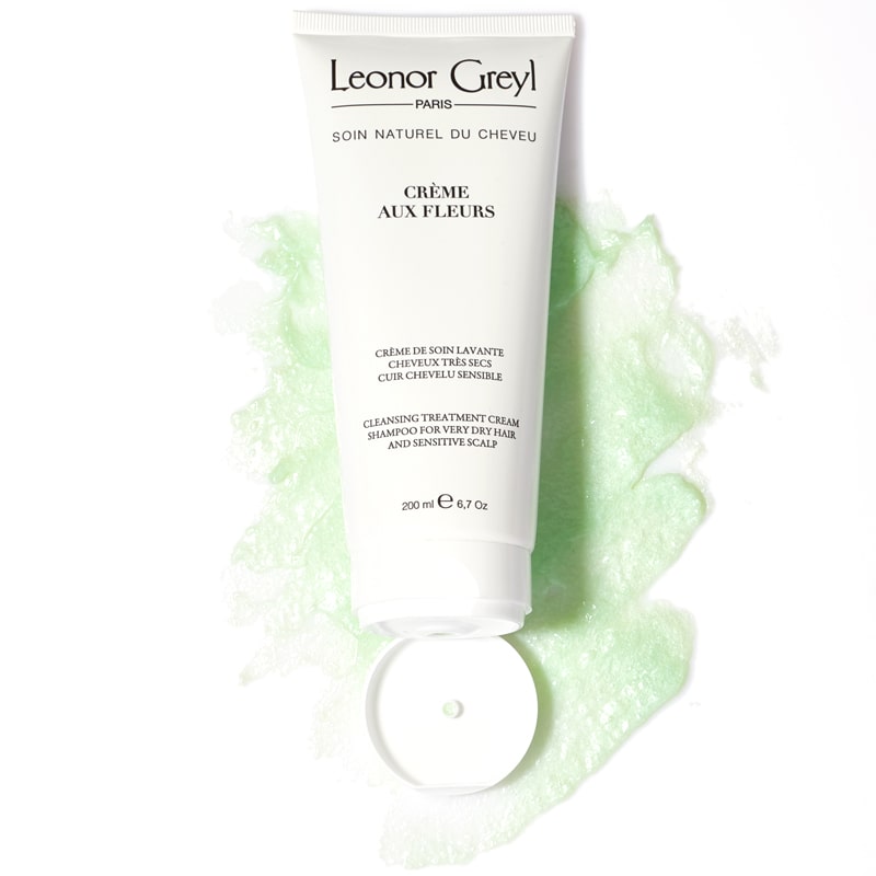 Lifestyle shot shown top view of Leonor Greyl Creme aux Fleurs Cream Washing Cream (200 ml) with swatch showing color and texture in the background