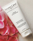 Lifestyle shot top view of Leonor Greyl Creme aux Fleurs Cream Washing Cream (200 ml) with pink rose petals in the background