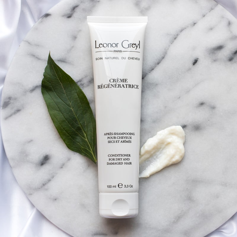 Lifestyle shot top view on marble of Leonor Greyl Creme Regeneratrice Conditioner (100 ml) with swatch and single leaf in the background