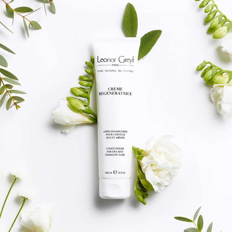 Lifestyle shot top view of Leonor Greyl Creme Regeneratrice Conditioner (100 ml) with white flowers and leaves in the background