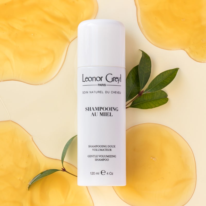 Lifestyle shot top view of Leonor Greyl Shampooing au Miel (120 ml) with honey and green leaves in the background