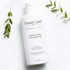 Lifestyle shot top view of Leonor Greyl Lait Lavant a la Banane Shampoo (200 ml) with leaves in the background