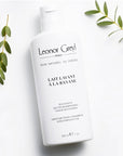 Lifestyle shot top view of Leonor Greyl Lait Lavant a la Banane Shampoo (200 ml) with leaves in the background