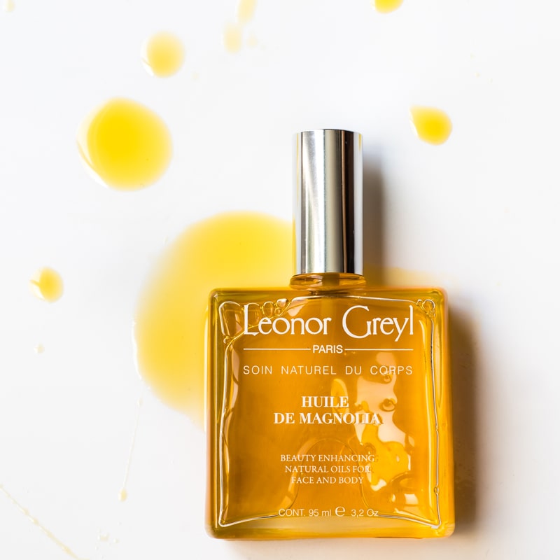 Lifestyle shot top view of Leonor Greyl Magnolia Beauty Oil (95 ml) with oil drops in the background