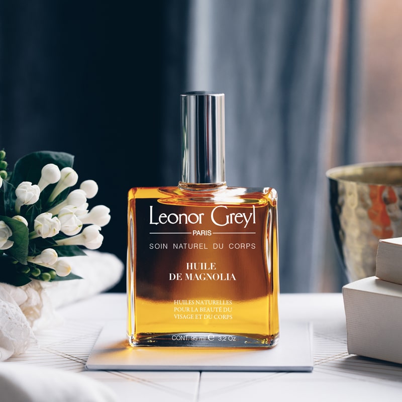Lifestyle shot of Leonor Greyl Magnolia Beauty Oil (95 ml) on desk with white flowers, vase and books in the background