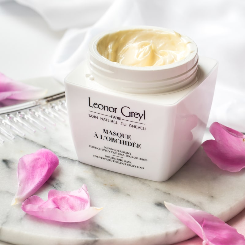 Lifestyle shot of Leonor Greyl Masque A L&#39;Orchidee (200 ml) with lid off showing color and texture of the masque and pink petals in the background