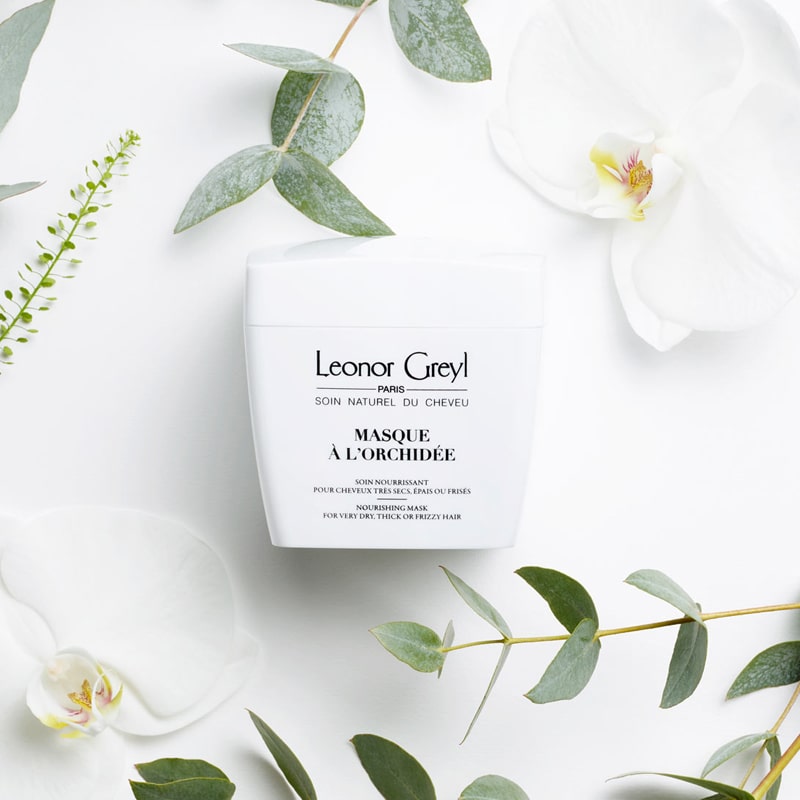 Lifestyle shot top view of Leonor Greyl Masque A L&#39;Orchidee (200 ml) with white orchids and leaves in the background