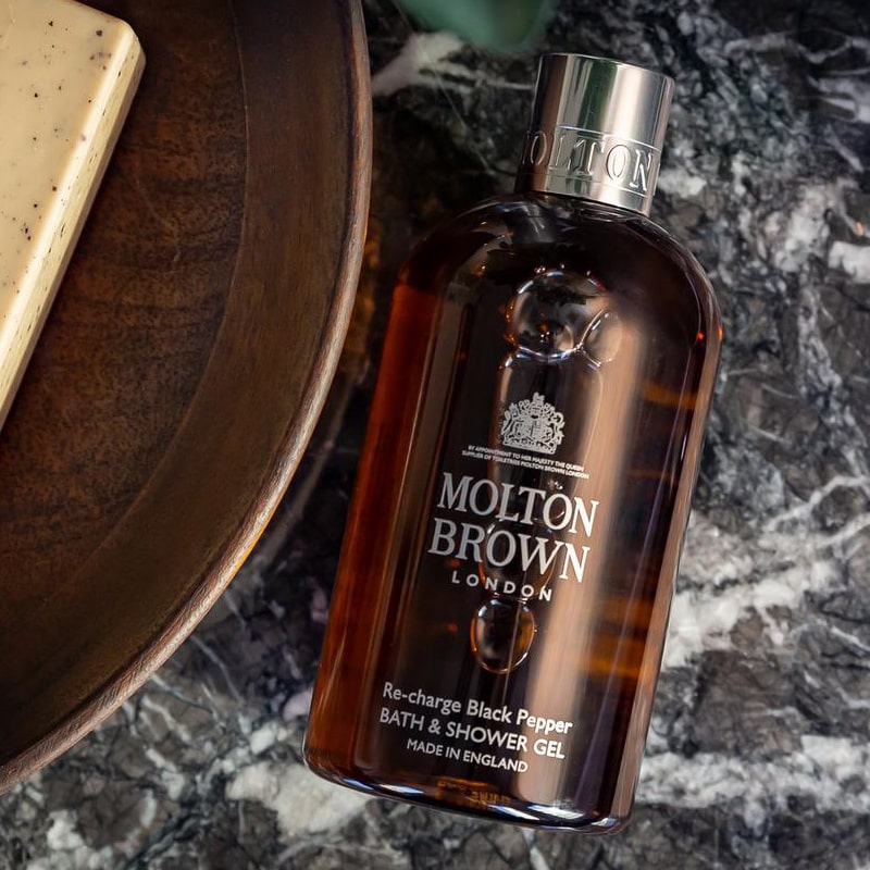 Lifestyle shot of Molton Brown Re-charge Black Pepper Bath &amp; Shower Gel (300 ml) with marble background