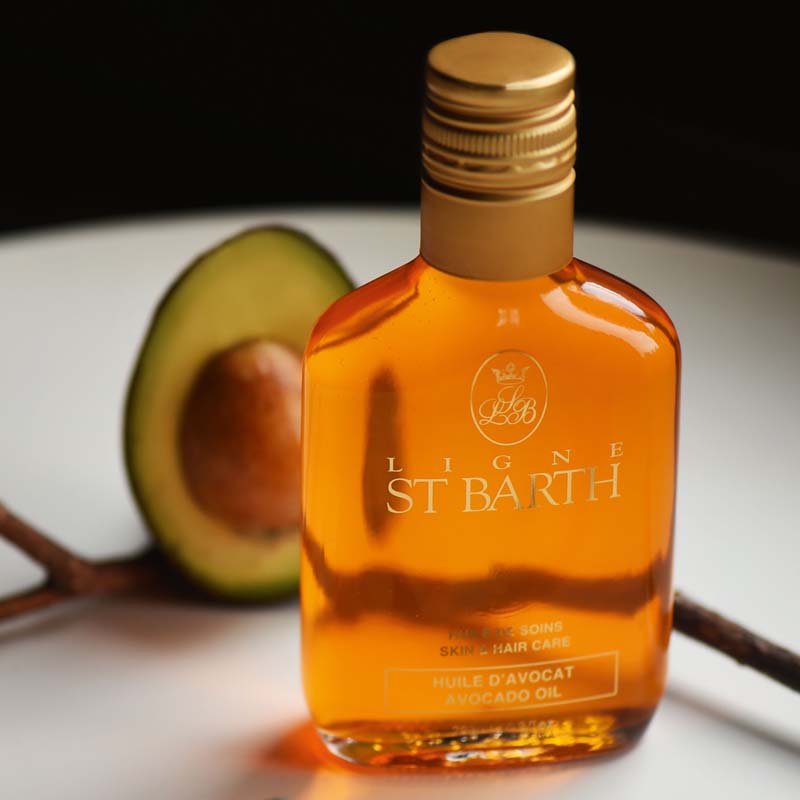 Lifestyle shot of Ligne St. Barth Avocado Oil (6.8 oz) with avocado in the background