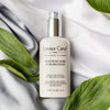 Lifestyle shot top view of Leonor Greyl Serum de Soie Sublimateur (75 ml) with white fabric and leaves in the background