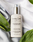 Lifestyle shot top view of Leonor Greyl Serum de Soie Sublimateur (75 ml) with white fabric and leaves in the background