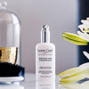 Lifestyle shot of Leonor Greyl Serum de Soie Sublimateur (75 ml) with white flowers, vase and brush in the background