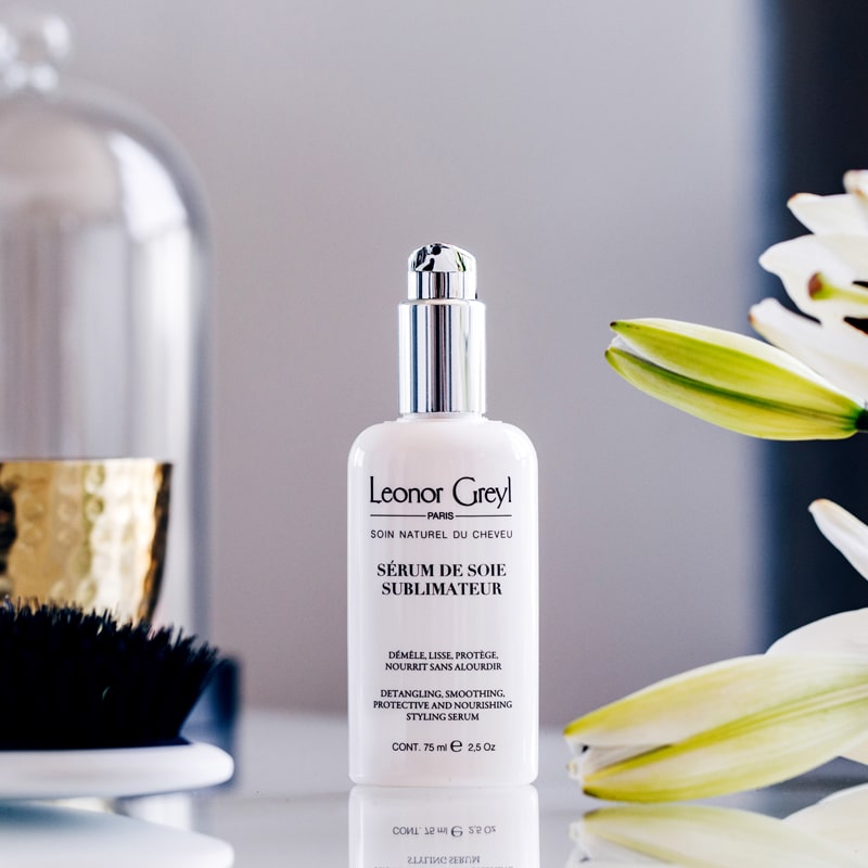 Lifestyle shot of Leonor Greyl Serum de Soie Sublimateur (75 ml) with white flowers, vase and brush in the background