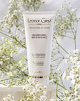 Lifestyle shot of Leonor Greyl Reviviscence Shampoo( 200 ml) with white flowers in the background