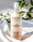 Lifestyle shot of Leonor Greyl Lait Luminescence Bi-Phase (150 ml) with white fabric and branch with leaves in the background