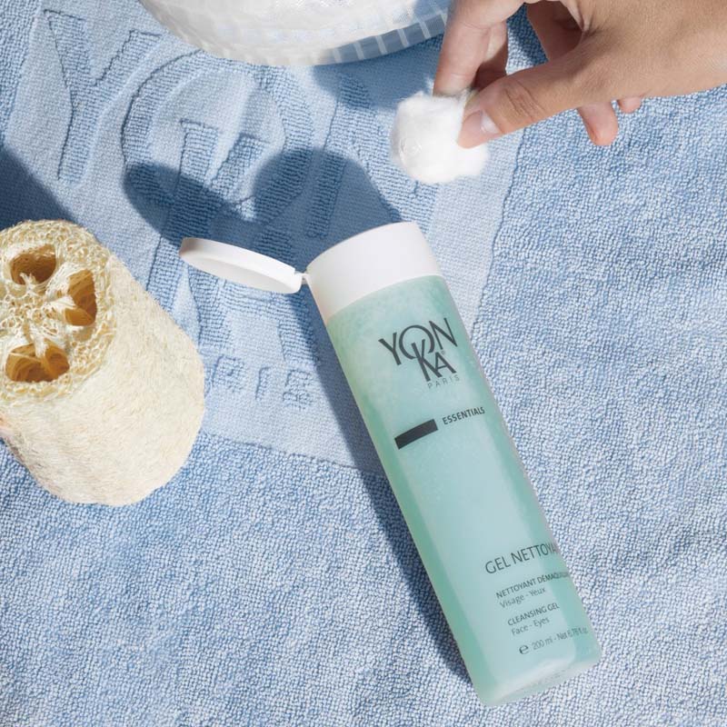 Lifestyle shot of Yon-Ka Paris Gel Nettoyant (200 ml) with model holding cotton ball near the top of the bottle with lid open 